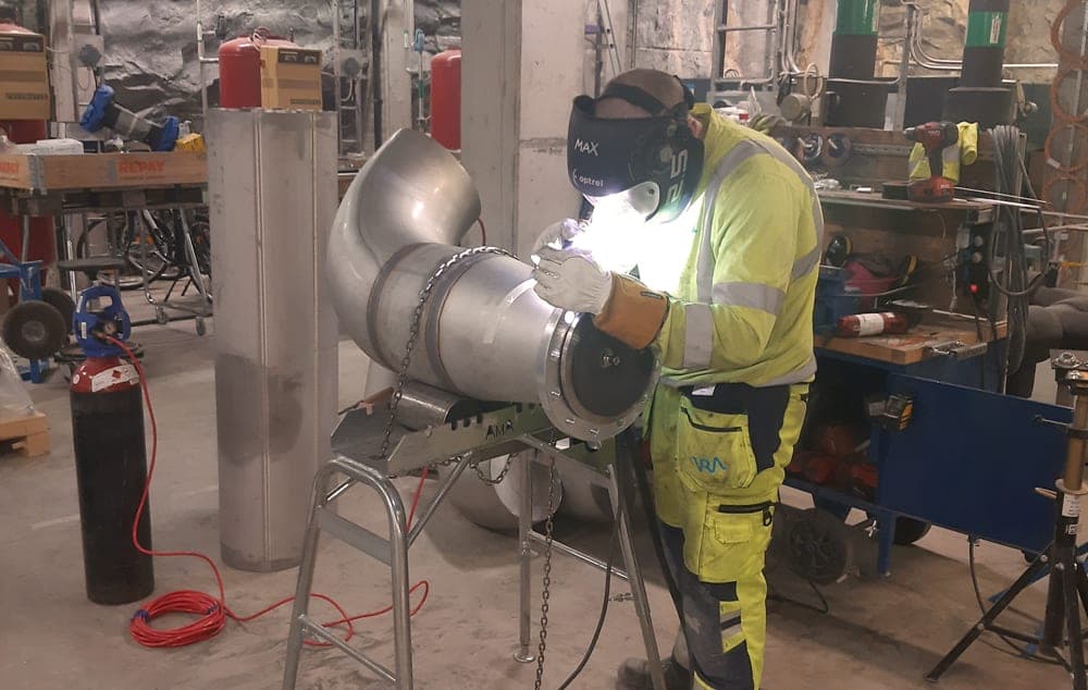 Max från VRA, i svetshjälm och varselkläder, svetsar på en grov rörböj